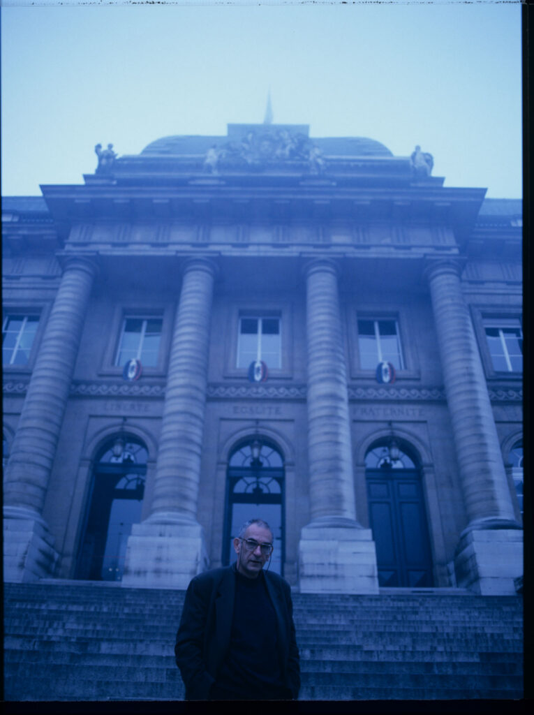 Krzysztof Kieślowski (reżyser) przed spowitym niebieskim światłm gmachem paryskiego Pałacu Sprawiedliwości.