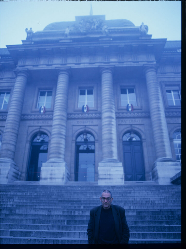 Krzysztof Kieślowski (reżyser) przed spowitym niebieskim światłm gmachem paryskiego Pałacu Sprawiedliwości.