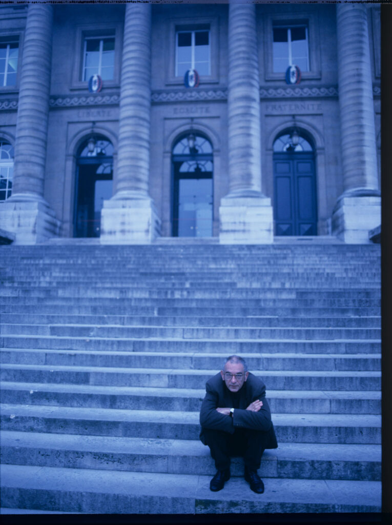 Krzysztof Kieślowski (reżyser) przed spowitym niebieskim światłm gmachem paryskiego Pałacu Sprawiedliwości.