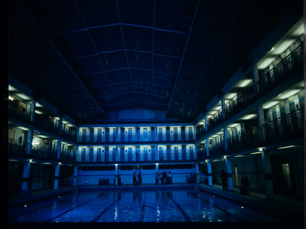 Ekipa na planie zdjęciowym na skąpanym w niebieskiej poświacie basenie Piscine Pontoise w Paryżu.